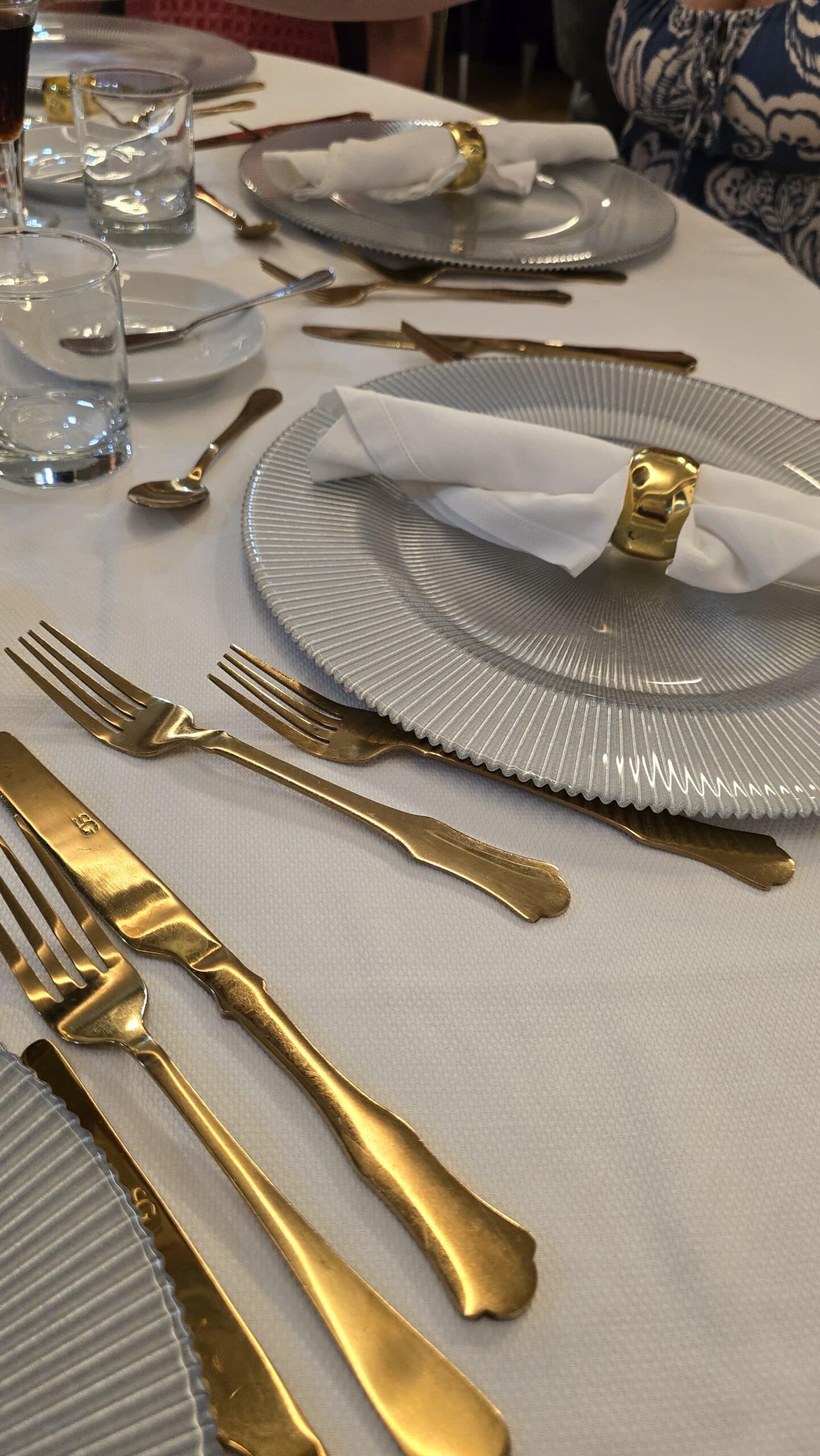 A formal dining table set with gold utensils, folded white napkins in gold rings, glassware, and elegant grey-rimmed plates evokes the sophistication on an Always Croatia cruise. 